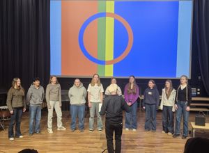 Elevar på musikklinja som syng samiske songar framfor eit bilete av samane sitt flagg