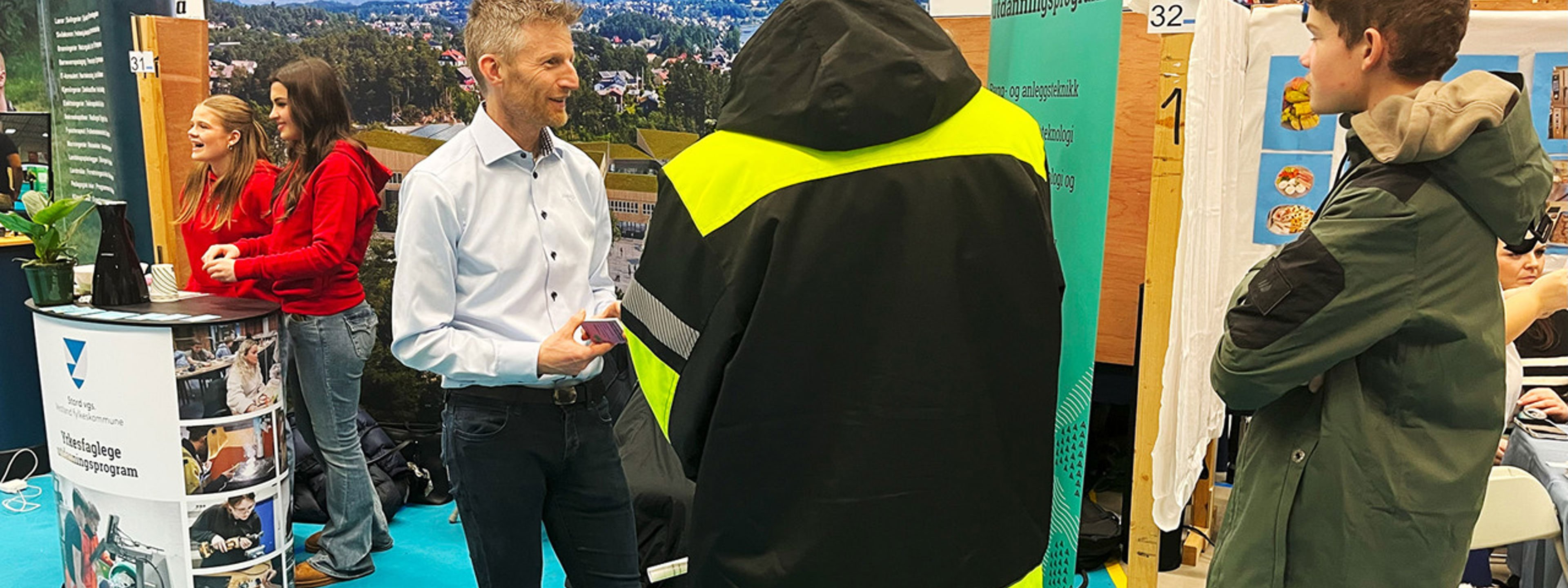 Ein lærar på utdanningsmessa som informerer om skulen sitt tilbod til to ungdomar